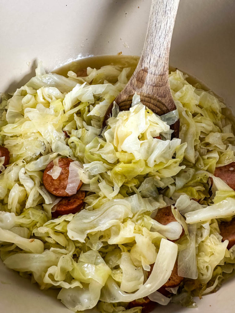 cooked cabbage and sausage in a pot with a wooden spoon