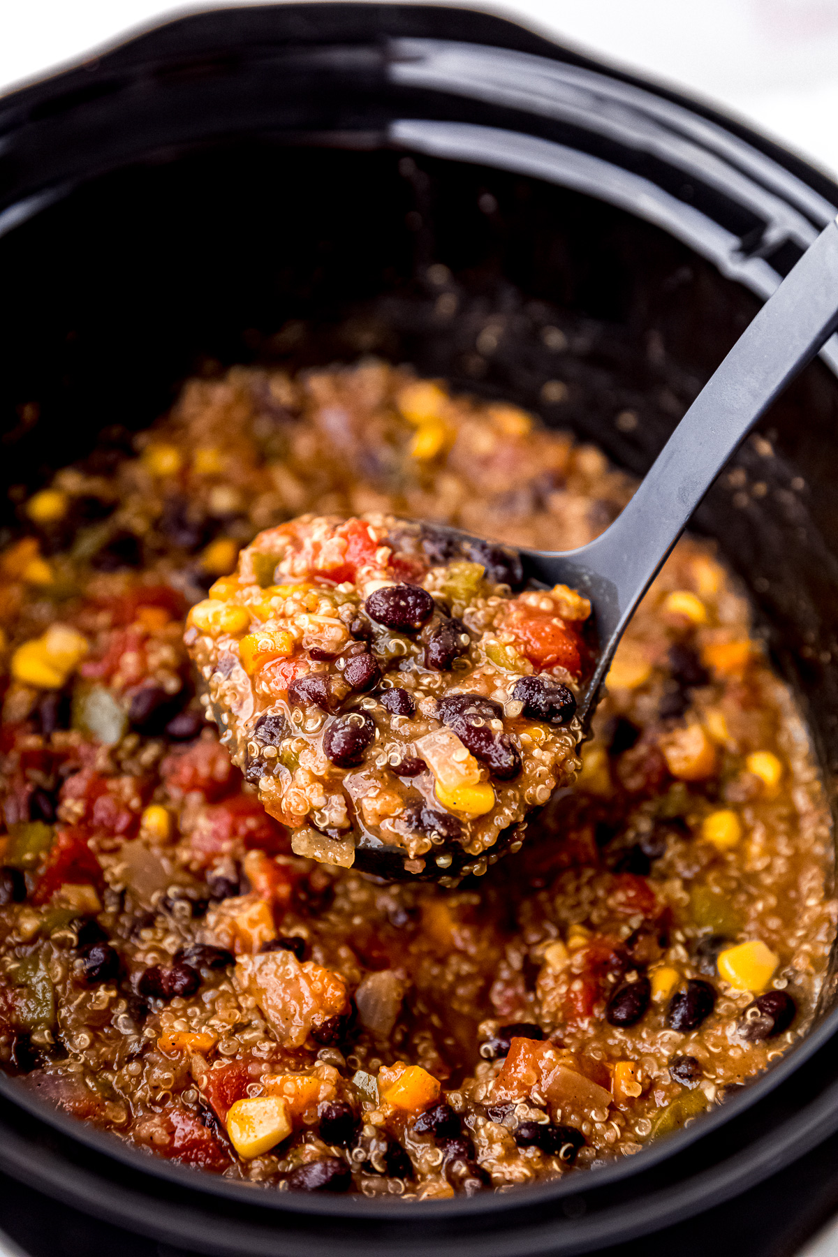 Close up of a full ladle of vegan chili above a slow cooker full of vegan chili