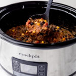 A slow cooker with a ladle pulling a spoonful of vegan chili out of it