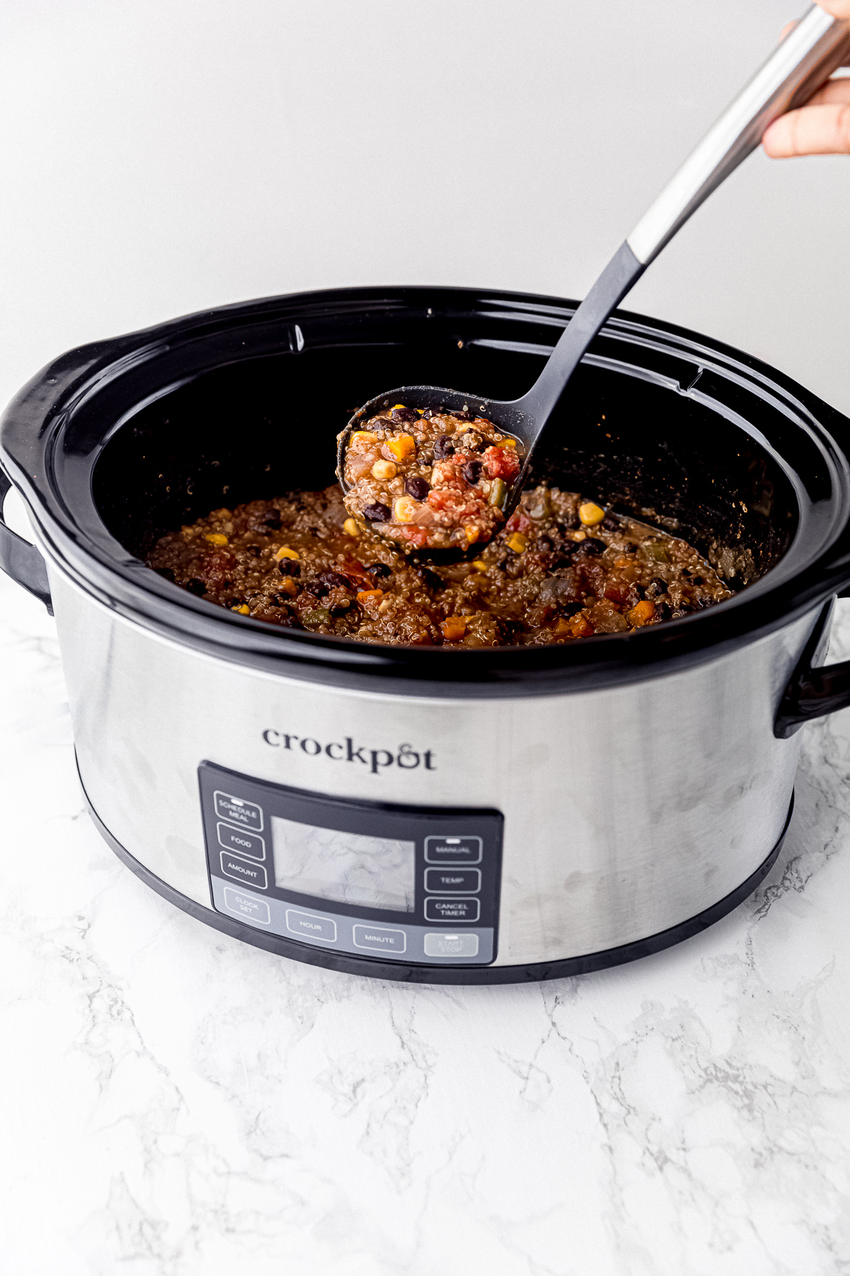 A slow cooker filled with vegan chili, with a ladle taking a serving out