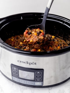 A slow cooker with a ladle pulling a spoonful of vegan chili out of it