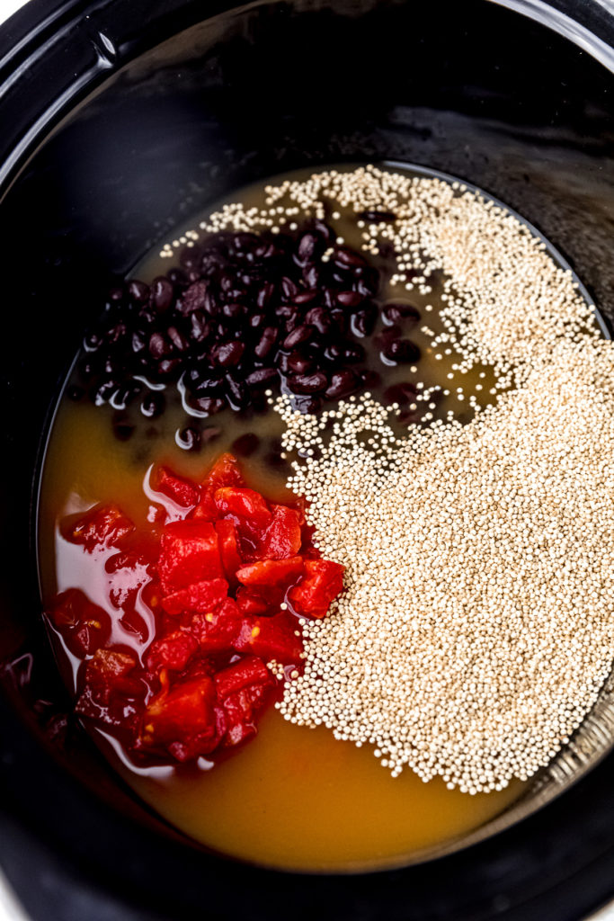 Canned tomatoes, black beans, uncooked quinoa, and vegetable broth in a slow cooker