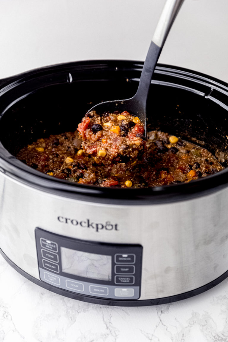 A slow cooker with a ladle pulling a spoonful of vegan chili out of it