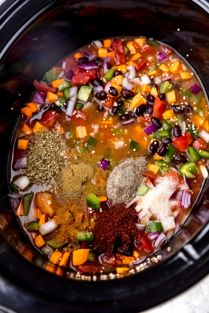 The base for vegan chili with a pile of seasonings on top, in a slow cooker