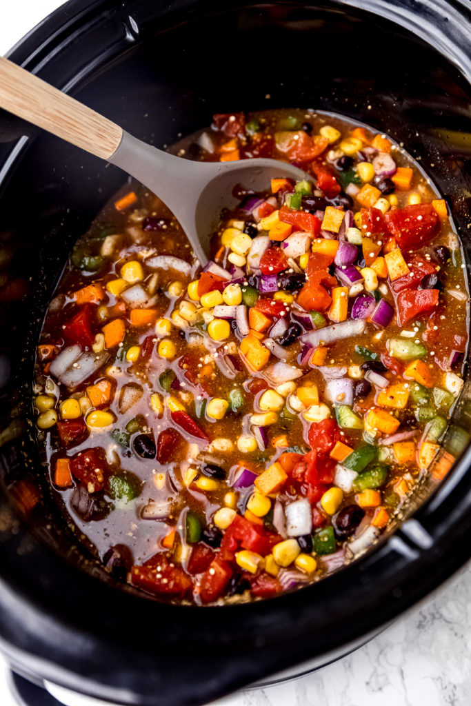 A spoon stirring uncooked vegan chili in a slow cooker
