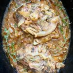 overhead shot of cooked Crockpot Pork Chops, Apples & Onions garnished with fresh thyme in a black slow cooker