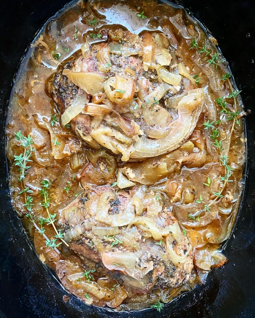 overhead shot of cooked Crockpot Pork Chops, Apples & Onions garnished with fresh thyme in a black slow cooker