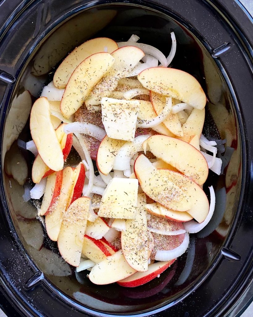 overhead shot of uncooked Crockpot Pork Chops, Apples & Onions in a black slow cooker