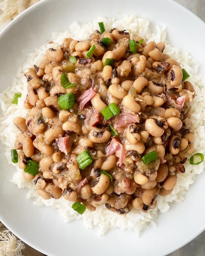 overhead shot of cooked hoppin john over rice in a white bowl garnished with sliced green onions