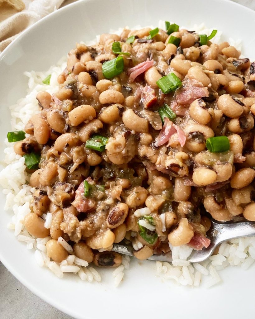 close up shot of overhead shot of cooked hoppin john over rice in a white bowl garnished with sliced green onions with a silver spoon