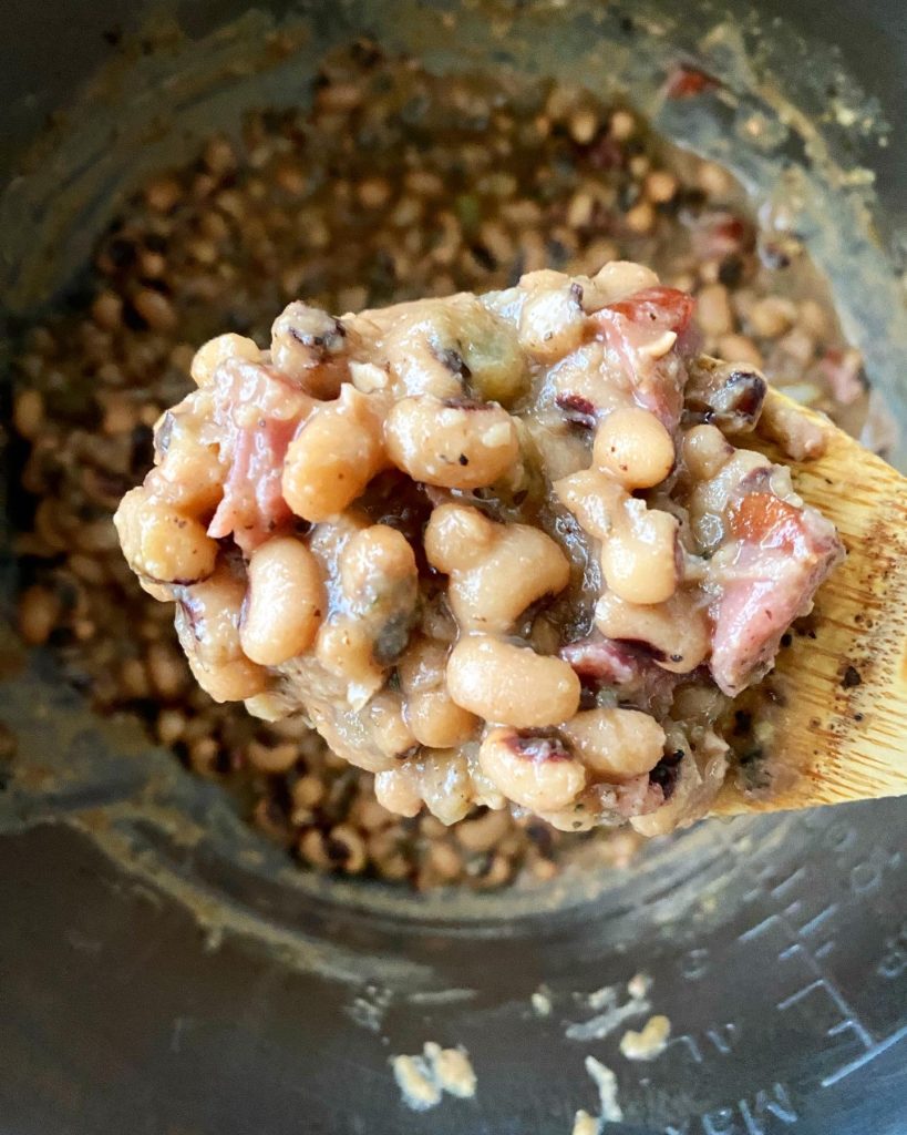 close up shot of cooked hoppin john on a wooden spoon over an instant pot