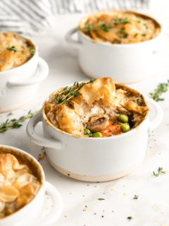 A pot pie in an individual ramekin, with a thyme sprig on top, surrounded by more pot pies and thyme sprigs