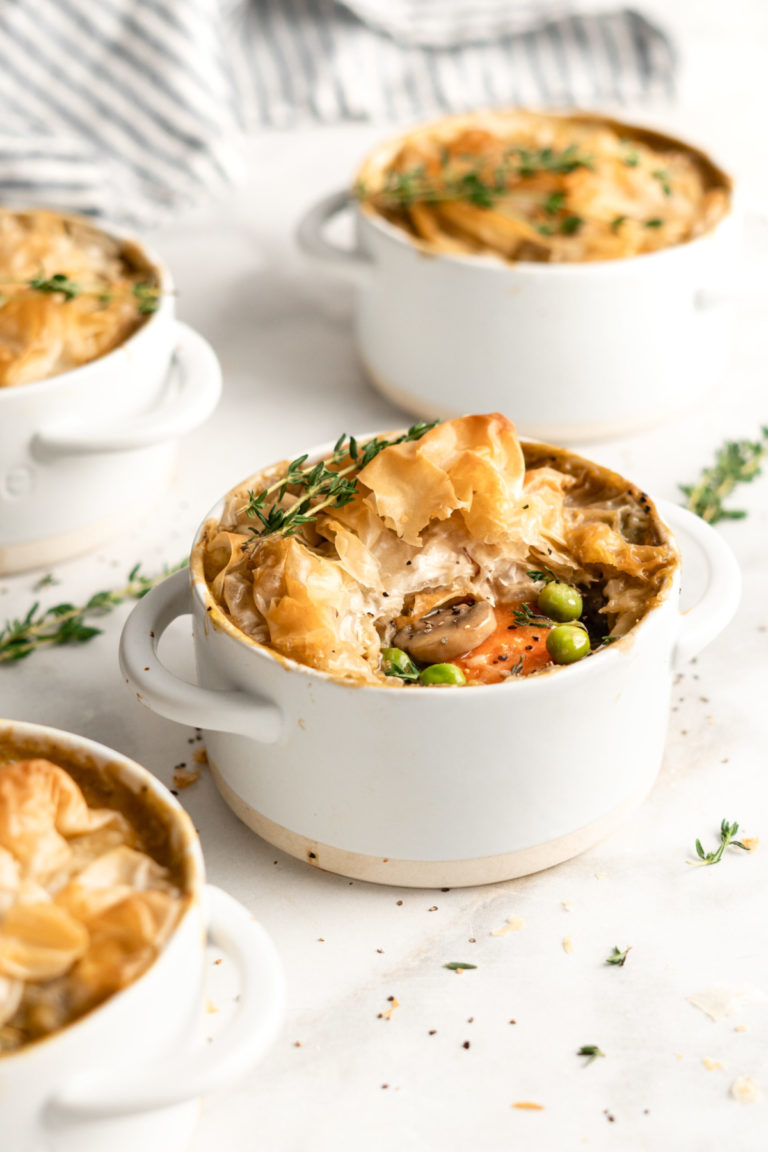 A pot pie in an individual ramekin, with a thyme sprig on top, surrounded by more pot pies and thyme sprigs