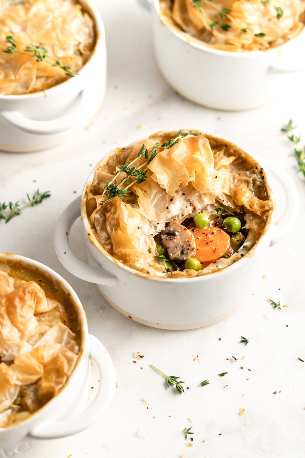 A pot pie with a sprig of thyme on top, next to three other pot pies