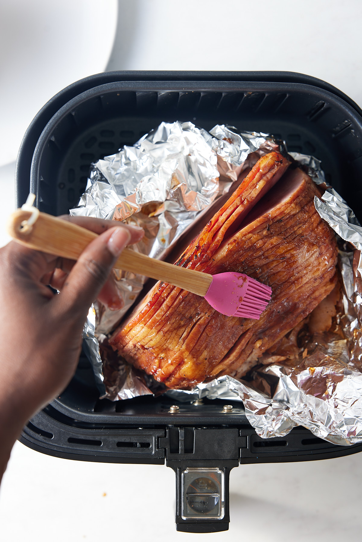 glaze being brished on ham in air fryer basket