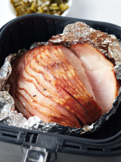 cooked ham in air fryer basket with greens in the background