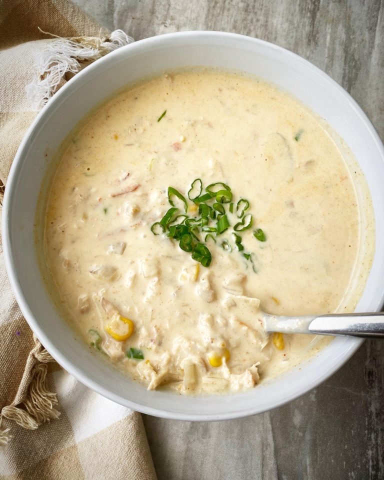 overhead shot of cooked corn & crab bisque in a white bowl garnished with sliced green onions