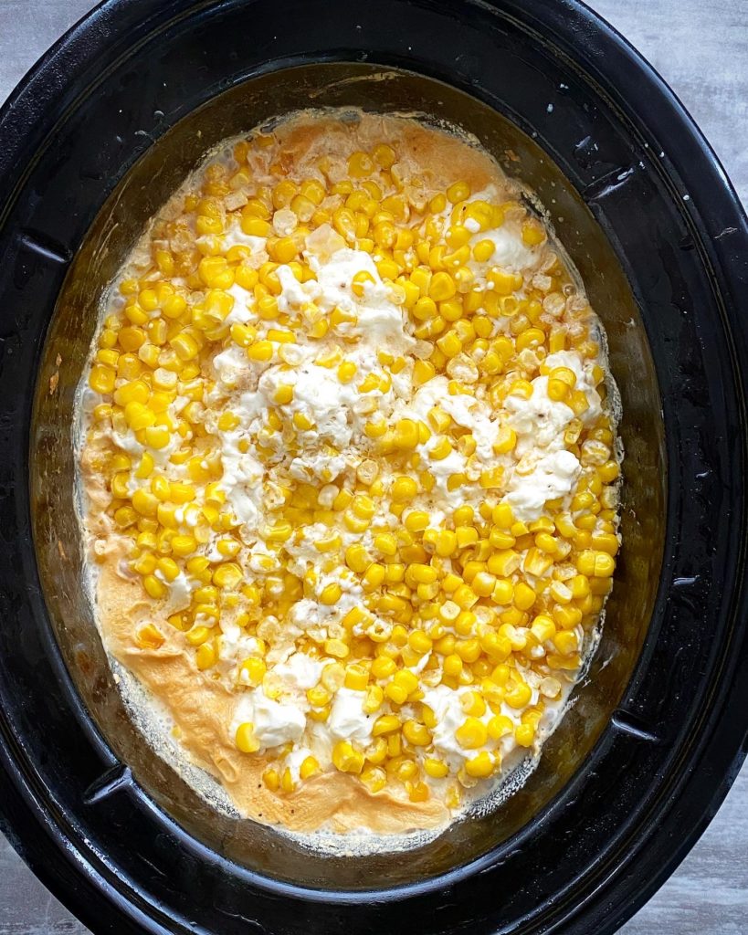 overhead shot of cooked creamed corn in a black slow cooker, unstirred