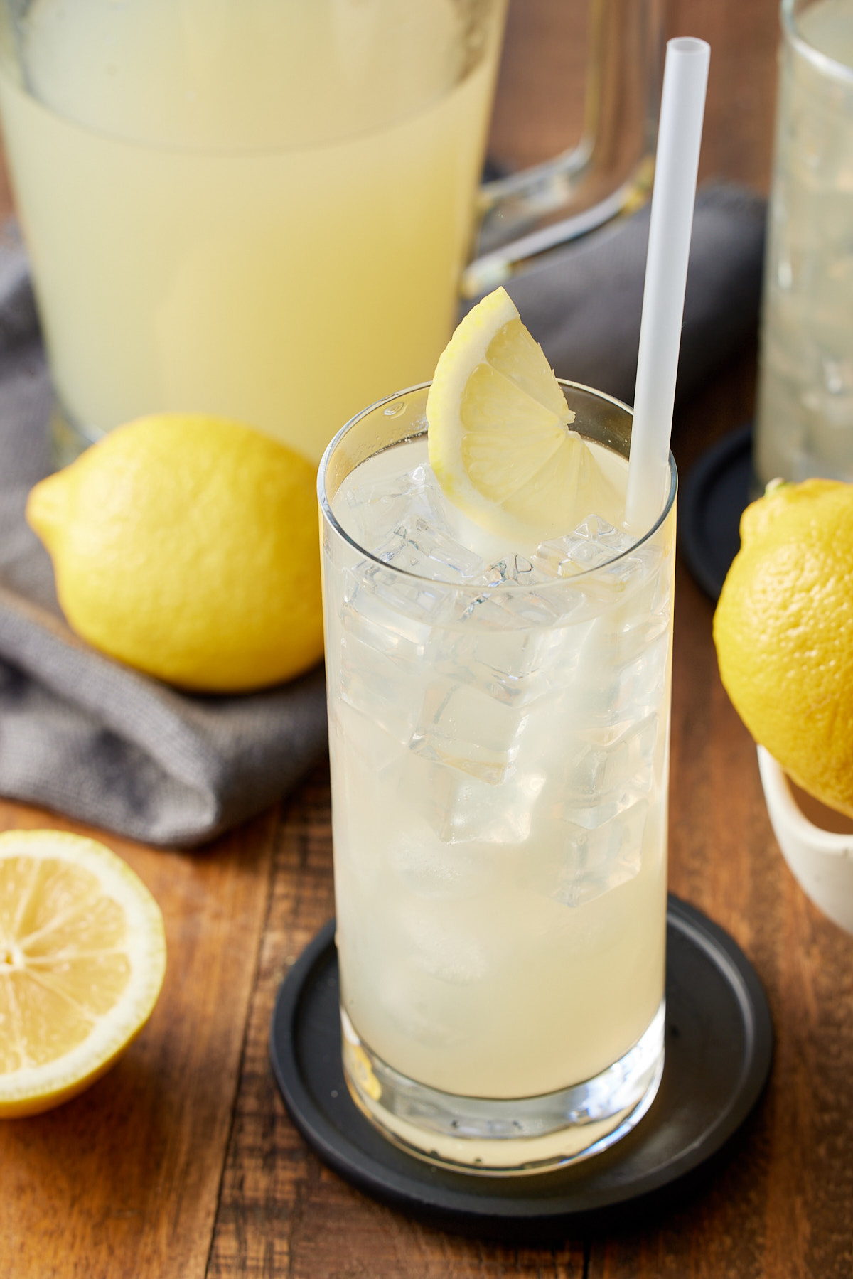 glass of lemonade in front of pitcher with whole lemons in background