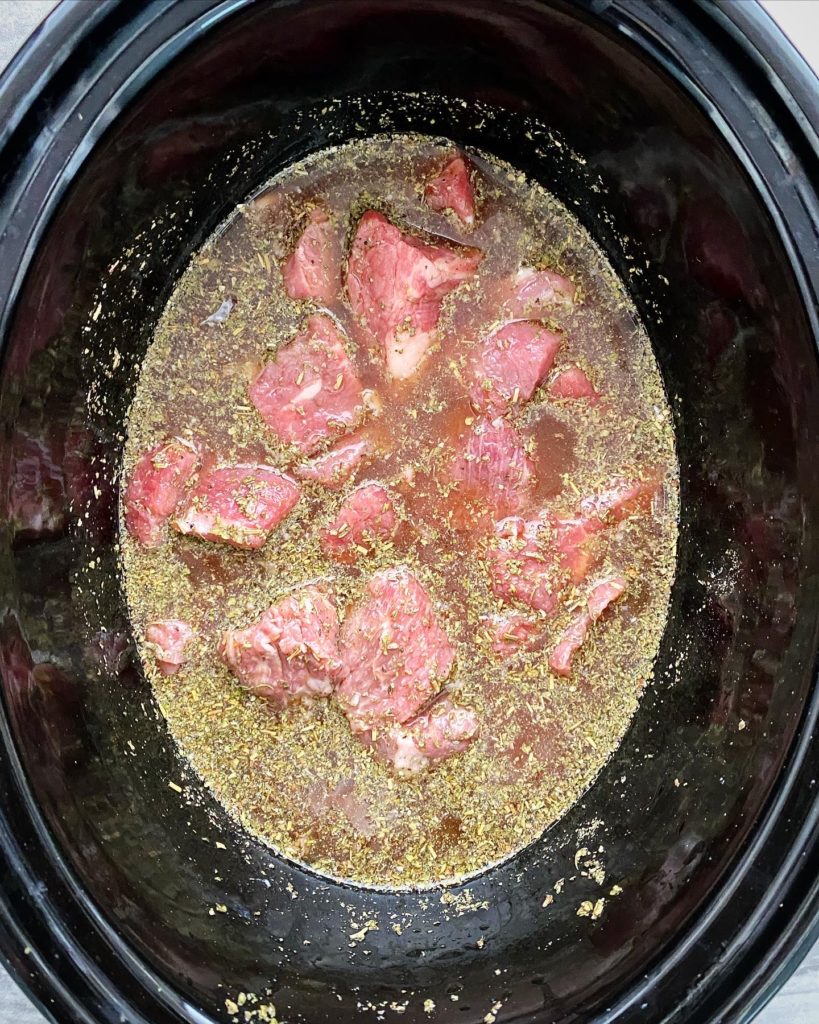 overhead shot of uncooked beef tips & gravy in a black slow cooker