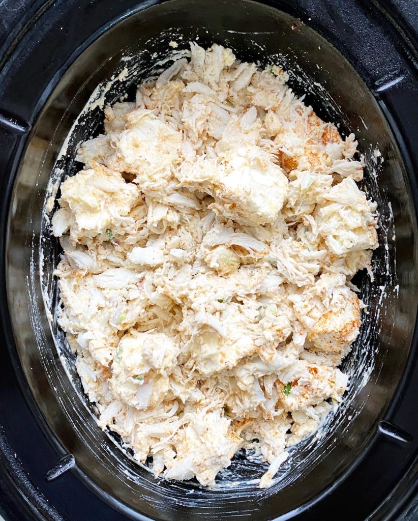 overhead shot of uncooked hot crab dip in a black slow cooker