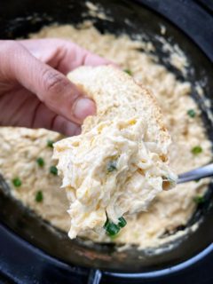 overhead shot of cooked hot crab dip in a black slow cooker with bread