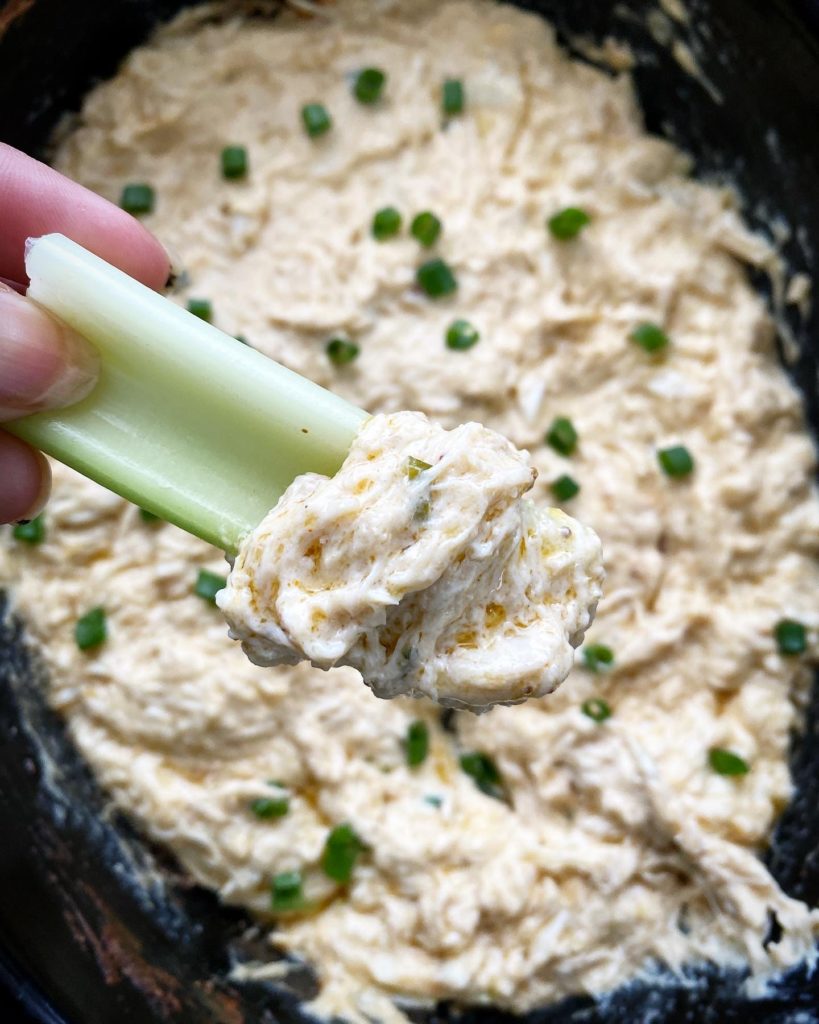 overhead shot of cooked hot crab dip in a black slow cooker with celery
