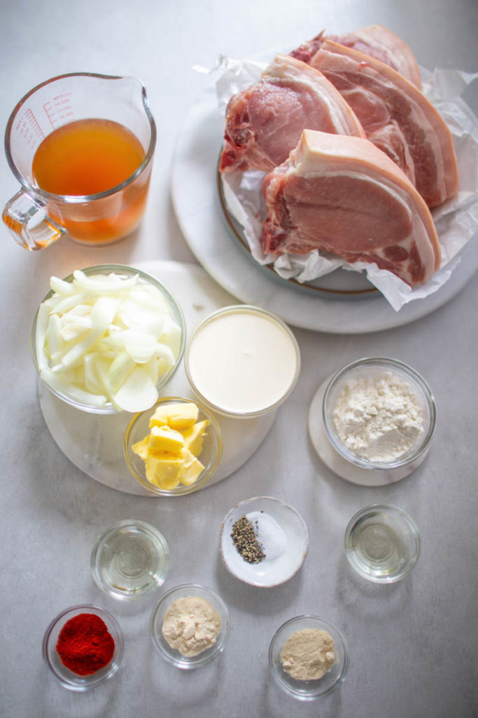 raw pork chops, onions, flour, spices, and broth in separate glass bowls
