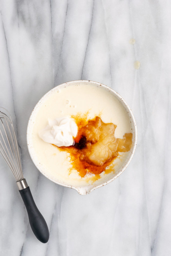 Overhead view of applesauce, vanilla, sour cream and wet ingredients in bowl