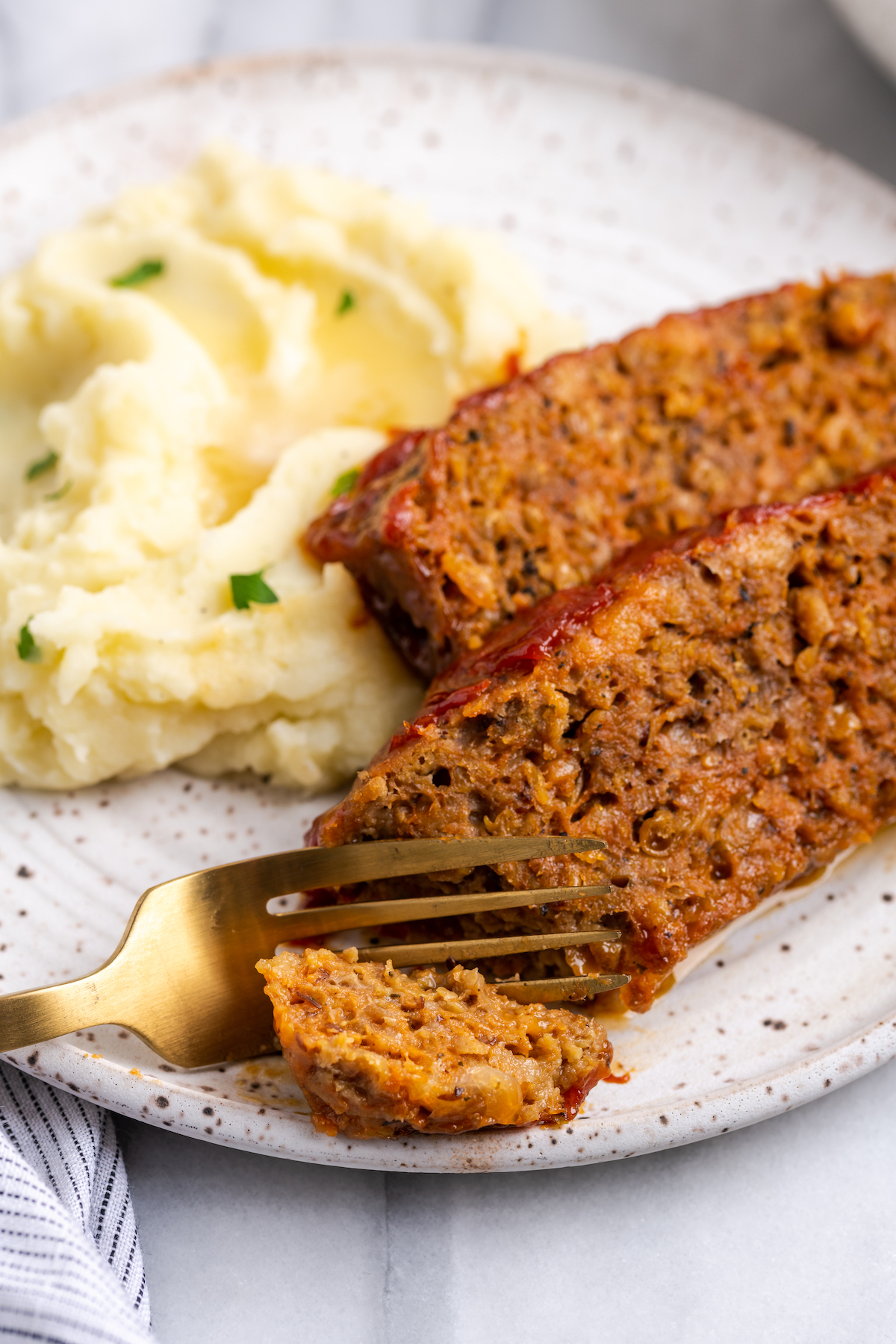 Fork cutting into vegan meatloaf on plate with mashed potatoes