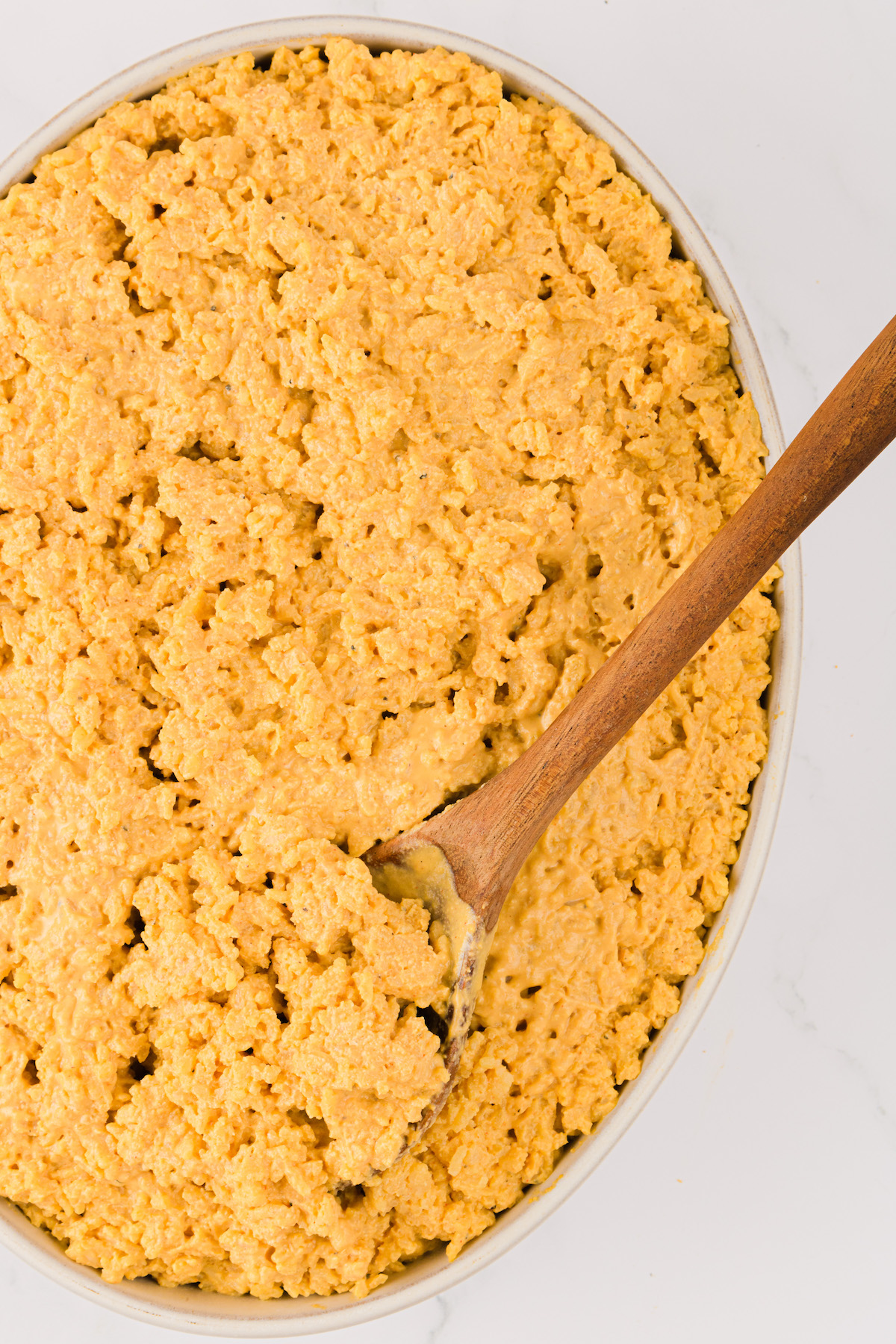 Overhead view of vegan cheesy rice in serving bowl with wooden spoon