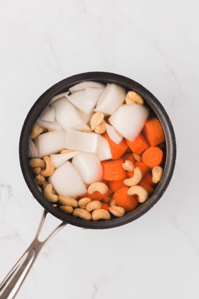 Overhead view of uncooked carrots, cashews, and onions in pot