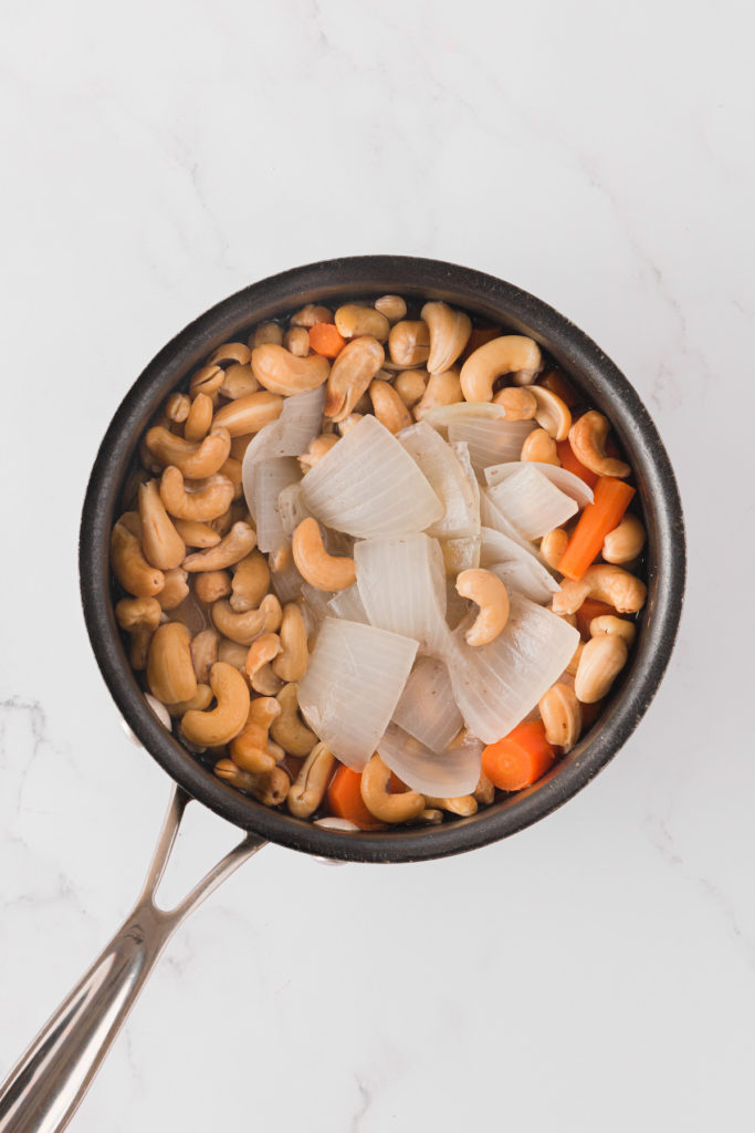 Overhead view of carrots, cashews, and onions in pot