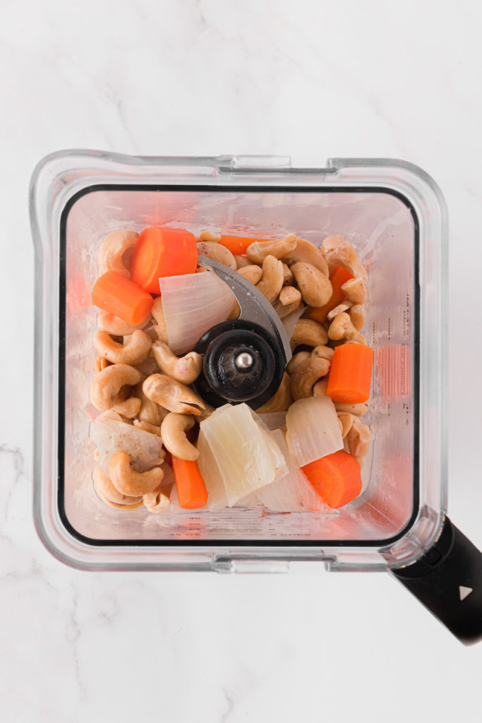 Overhead view of carrots, cashews, and onions in blender