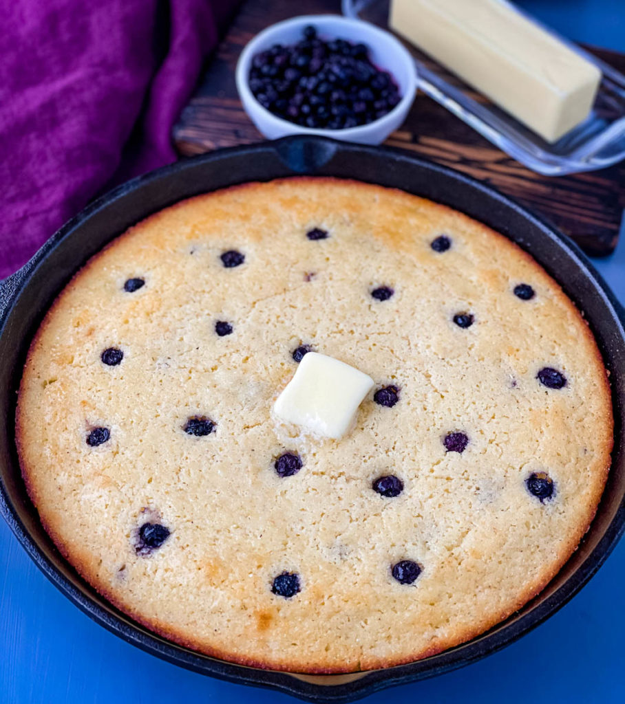 baked blueberry cornbread in a cast iron skillet topped with melted butter