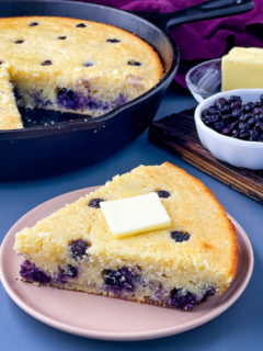 a slice of baked blueberry cornbread on a plate topped with melted butter