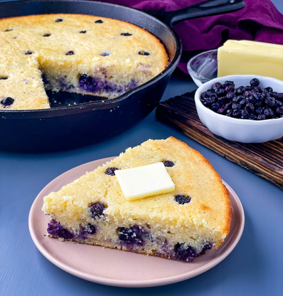 a slice of baked blueberry cornbread on a plate topped with melted butter