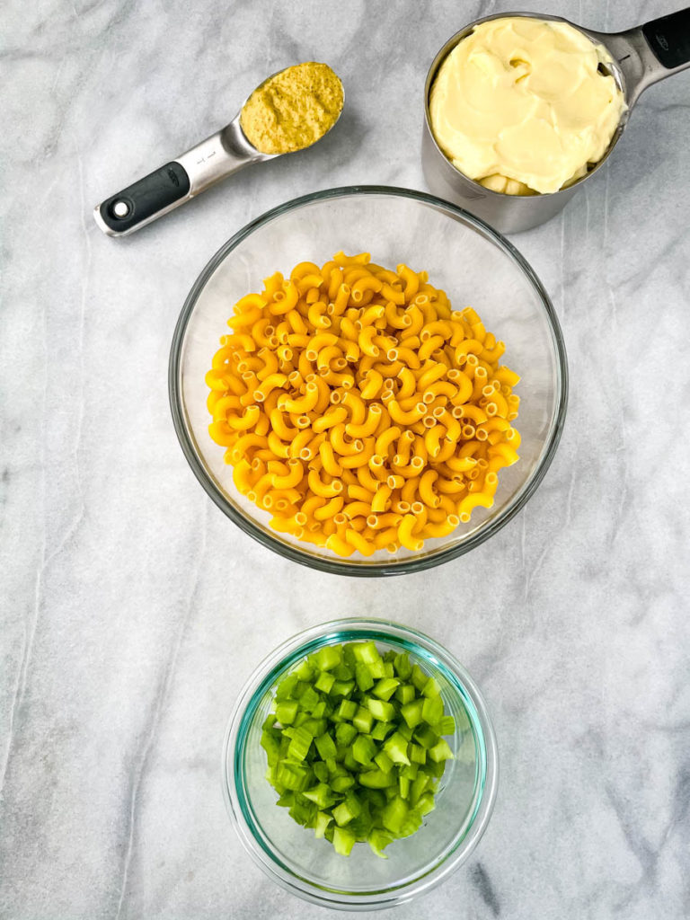 dry elbow macaroni pasta, mayo, mustard, and celery in separate bowls