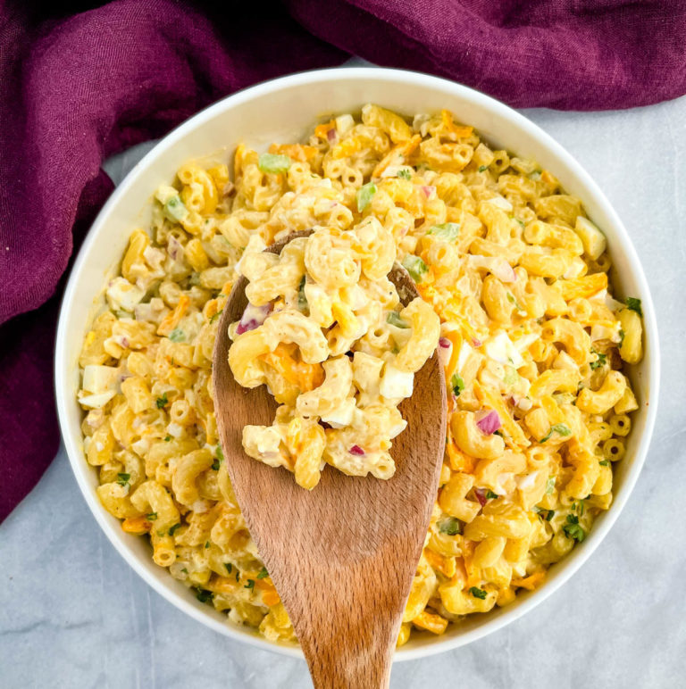 macaroni salad in a white bowl with a wooden spoon