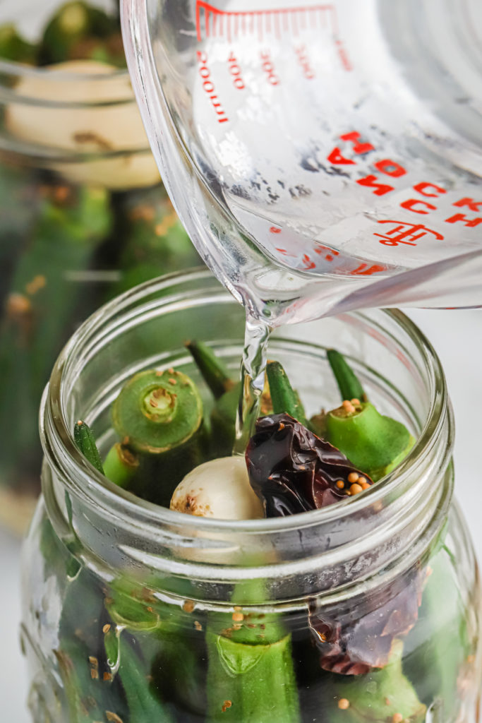 Pouring warm pickling liquid over a jar of okra.