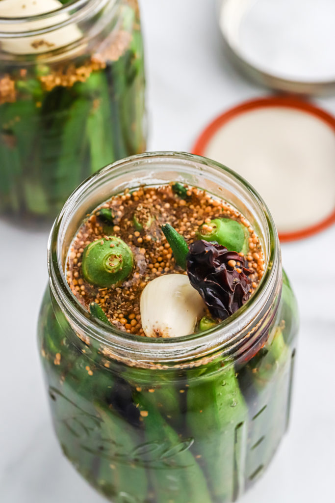 Herbs and spices on top of okra in a pint jar.