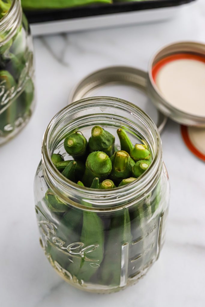 Washed okra pods packed into a pint jar.