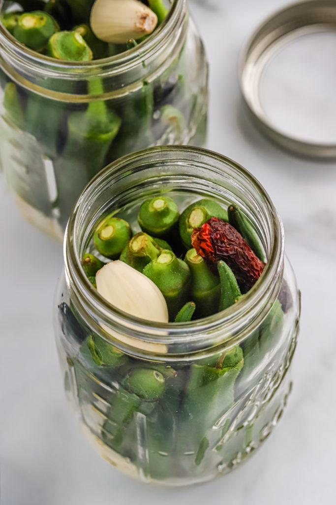 Herbs and spices on top of okra in a pint jar.