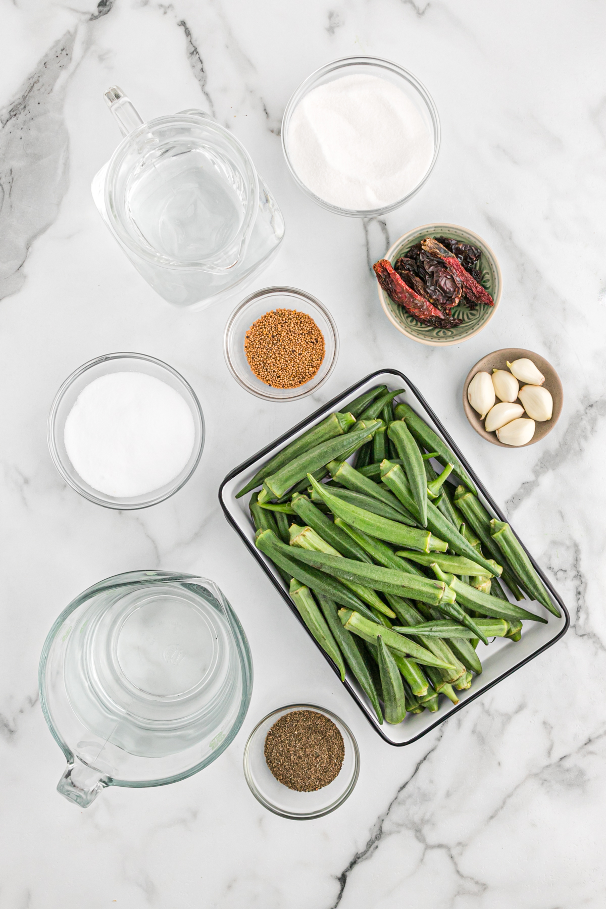 Ingredients for pickled okra in bowls on a white counter.