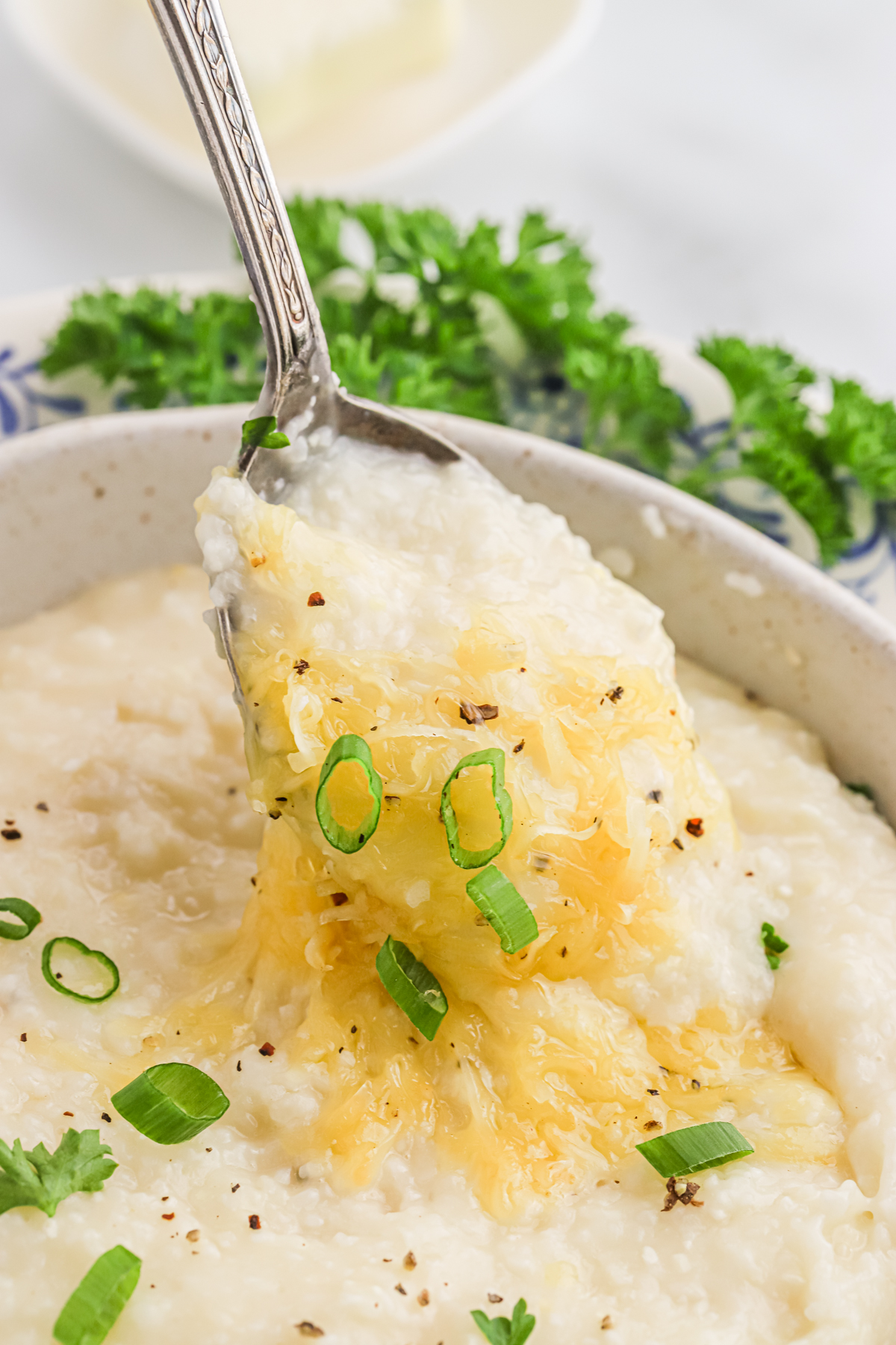 A spoon pulling out a bite of cheesy gouda grits from a bowl.