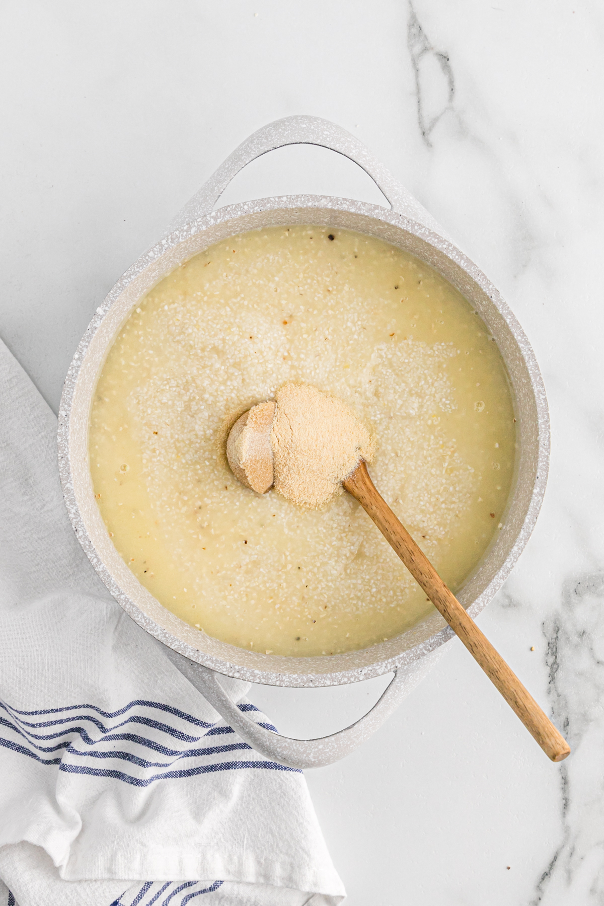 Brown sugar and seasoning being stirred into a pot of grits.