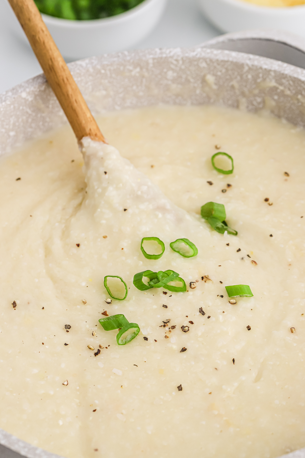 Green onions on top of a pot of cheesy smoked gouda grits.