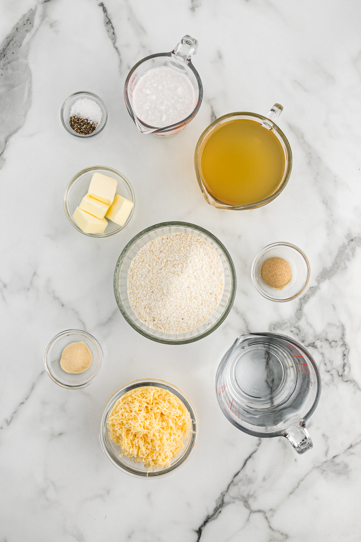 Ingredients for cheesy grits in bowls on a white counter.