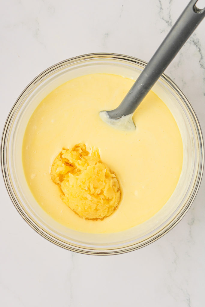 Overhead view of crushed pineapple added to glass mixing bowl of frosting