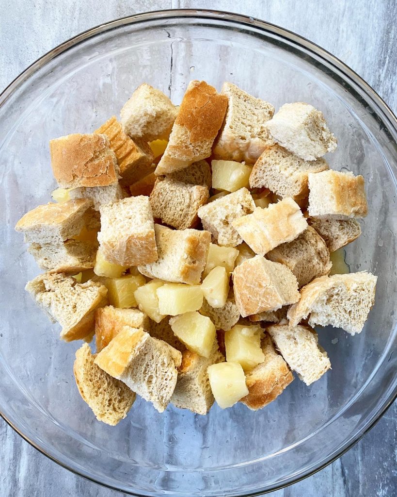 overhead shot of pineapple chunks and pieces of French bread in a glass bowl 
